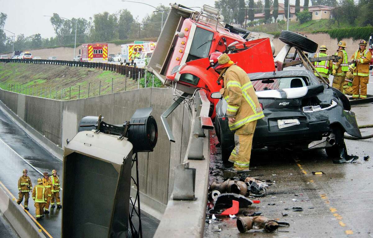 Crews keep an eye on a trailer on the westbound 91 Freeway after the driver of a two-trailer dirt-hauling dump truck slid, tipped and wound up partially dangling off the ramp Friday, in Anaheim, Calif.