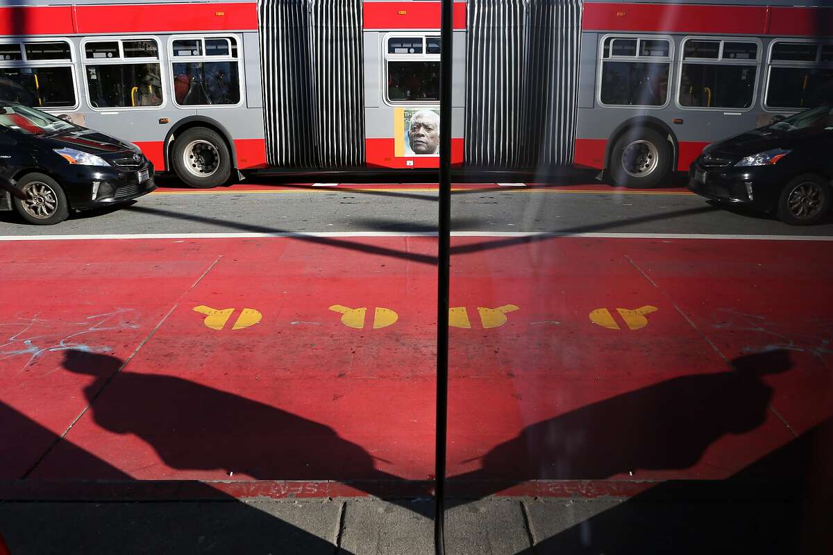 A bus using one of the red transit-only lanes and a car driving in the center of the lanes is seen reflected in a sign at 16th and Mission St on Friday, December 16 2016 in San Francisco, Calif.