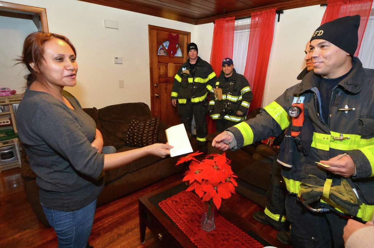 Firefighter George Baez presents gift cards on Wednesday December 21, 2016 to Yosely Lopez, the widow of Belarmino Lima who died earlier this year in Norwalk Conn. after being crushed in his driveway under a truck he was working on. Norwalk Firefighters are making a donations for food and services and toys for the childern to the Lima family,