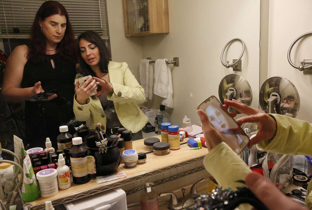 Billie Lynn, left, looks at a reference photograph pulled up by her longtime family friend Serenity Polizzi for Polizzi to use while doing Lynn's makeup as Lynn and her partner get ready in Lynn's home for her company SAP's formal themed holiday party Dec. 17, 2016 in San Jose, Calif.