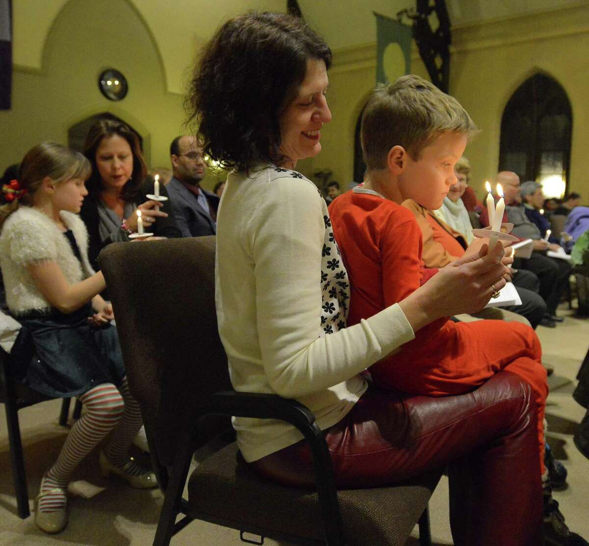 Basil Lintern, 7, of Stamford sits on the lap of his mother, Celeste Frye-Lintern, as they hold lighted candles as part of a Christmas Eve service. The Unitarian Universalist Congregation in Stamford holds "Fear Not Good News, Great Joy, For All People," a "Christmas Eve Carol" and candlelight service in Stamford on Dec.24, 2016.