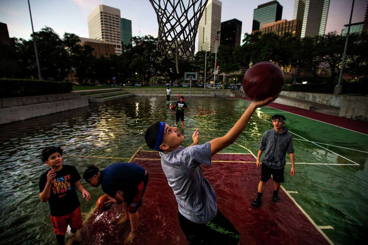 Angel Charles, 13, drives to the hoop as he and his friends play basketball in a court filled with rainwater from the morning's storms outside the Toyota Center.