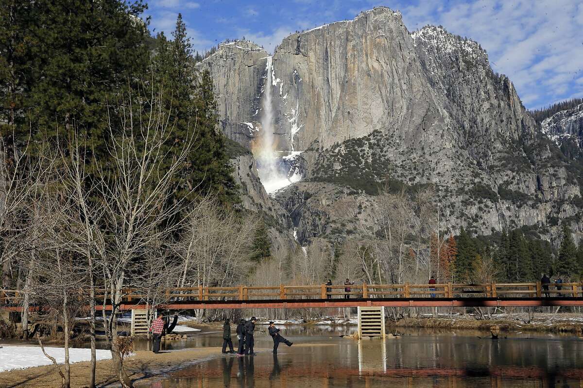 Visitors play along the Merced River with Yosemite Falls in the Yosemite National Park on Friday Jan. 6, 2017, where weather forecasters are expecting a huge storm to hit the valley over the next three days.