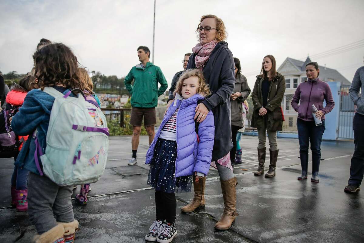 Aoife O'Dwyer, 7 (center), rests on her mother Kendra O'Dwyer as she waits in line before entering school in San Francisco, Calif., on Monday, Jan. 9, 2017.