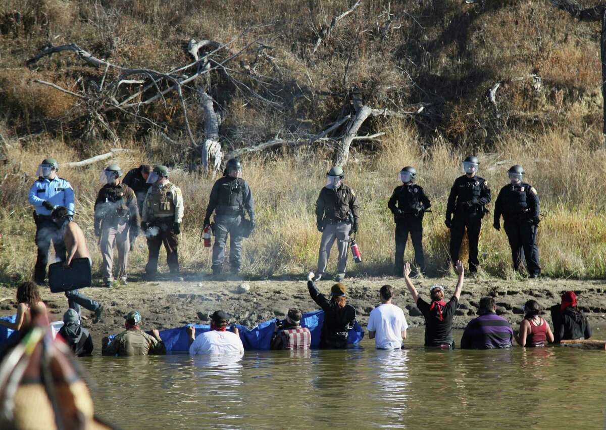 FILE - In this Nov. 2, 2016 file photo, protesters demonstrating against the expansion of the Dakota Access Pipeline wade in cold creek waters confronting local police near Cannon Ball, N.D. The cost of policing the Dakota Access pipeline protests in North Dakota is at least $22 million Â?— more than $5 million more than the state set aside last year. Protest-related funding decisions will be made by state lawmakers during the 2017 session. Leaders of the House and Senate appropriation committees say more funding will be approved, though the amount and method isn't known. (AP Photo/John L. Mone, File)