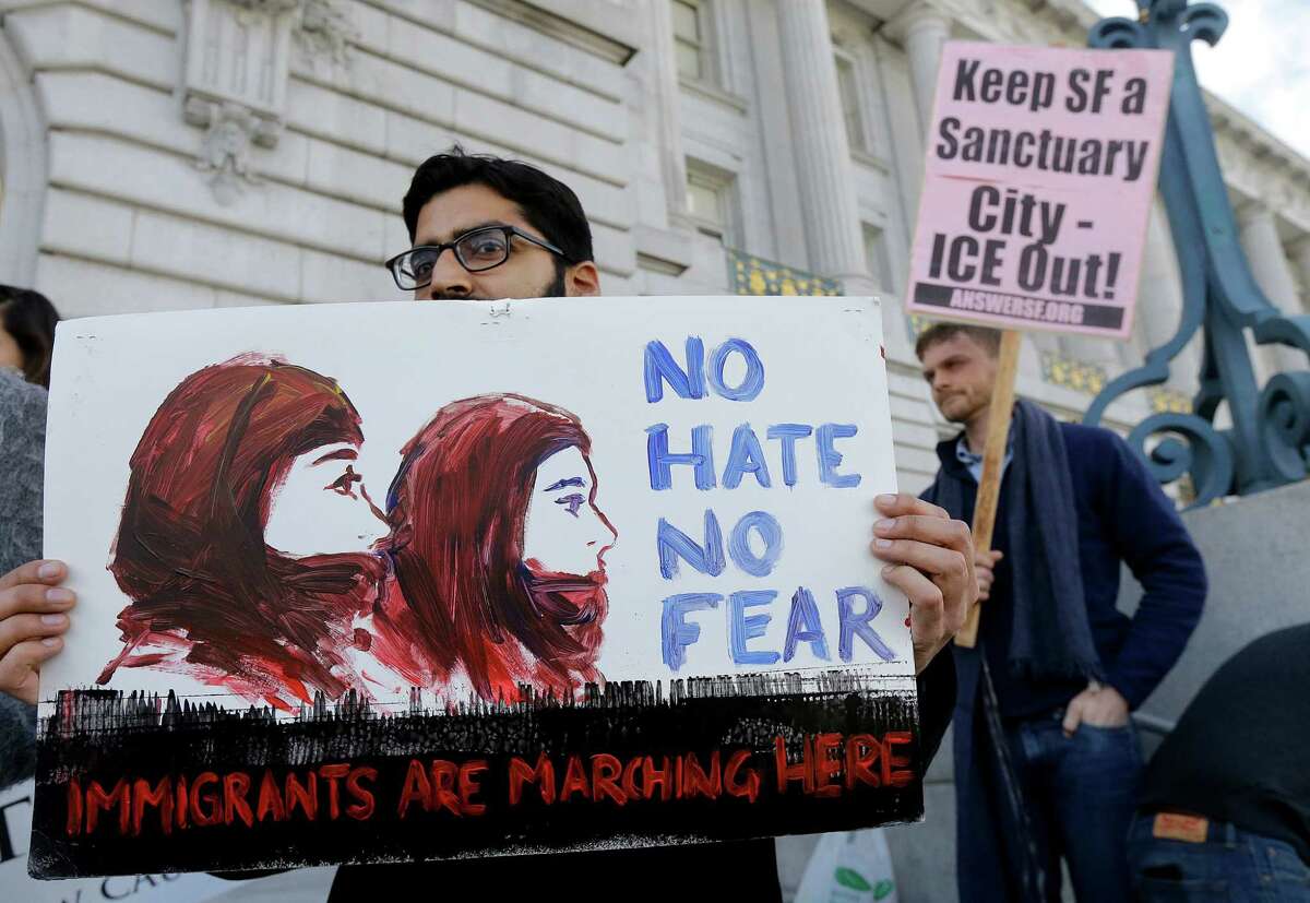 Anirvan Chatterjee, left, of the Alliance of South Asians Taking Action, holds a sign at a rally outside of City Hall in San Francisco, Wednesday, Jan. 25, 2017. President Donald Trump moved aggressively to tighten the nation's immigration controls Wednesday, signing executive actions to jumpstart construction of his promised U.S.-Mexico border wall and cut federal grants for immigrant-protecting "sanctuary cities." (AP Photo/Jeff Chiu)