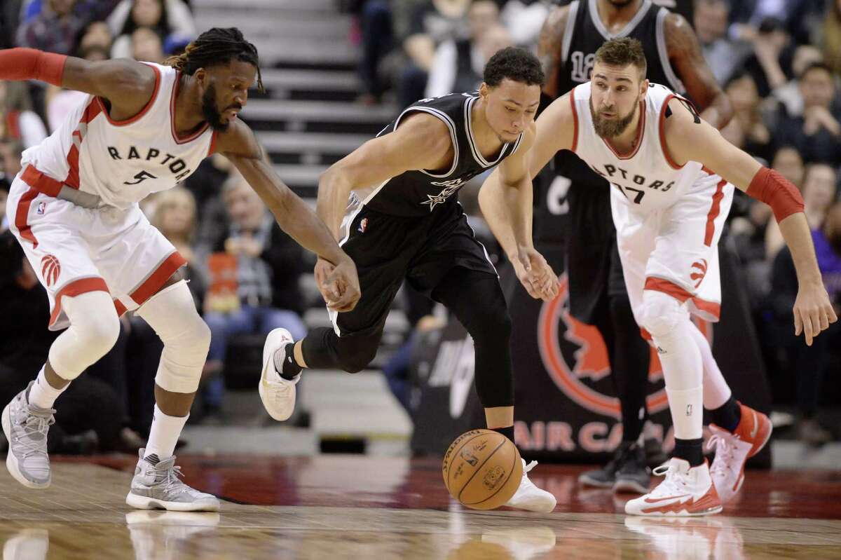 Raptors forward DeMarre Carroll (left) and center Jonas Valanciunas (right) hold on to the arms of Spurs guard Bryn Forbes as they chase a loose ball during the first half on Jan. 24, 2017, in Toronto.