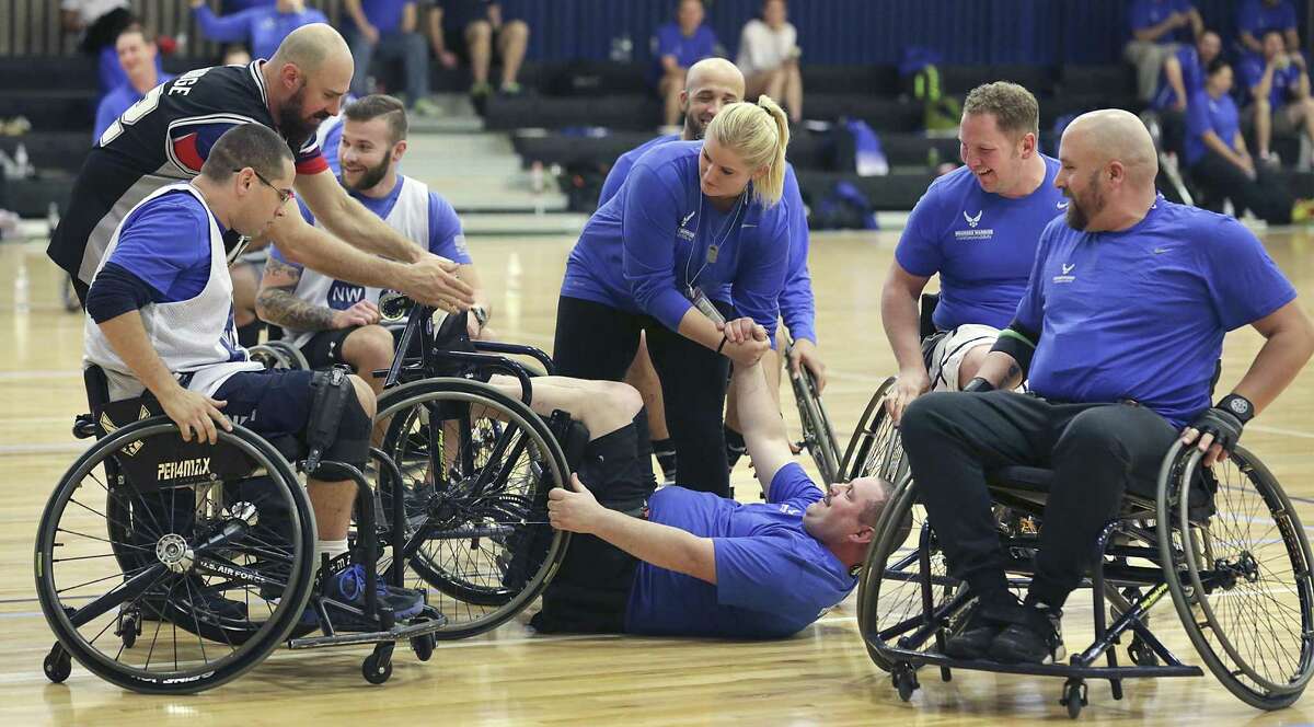 Smiling team mates come to the aid of a smiling tipped over wheelchair basketball player during an exhibition game at the Air Force Wounded Warrior Program Warrior Care Event at Joint Base San Antonio-Randolph on Friday, Jan. 13, 2017.