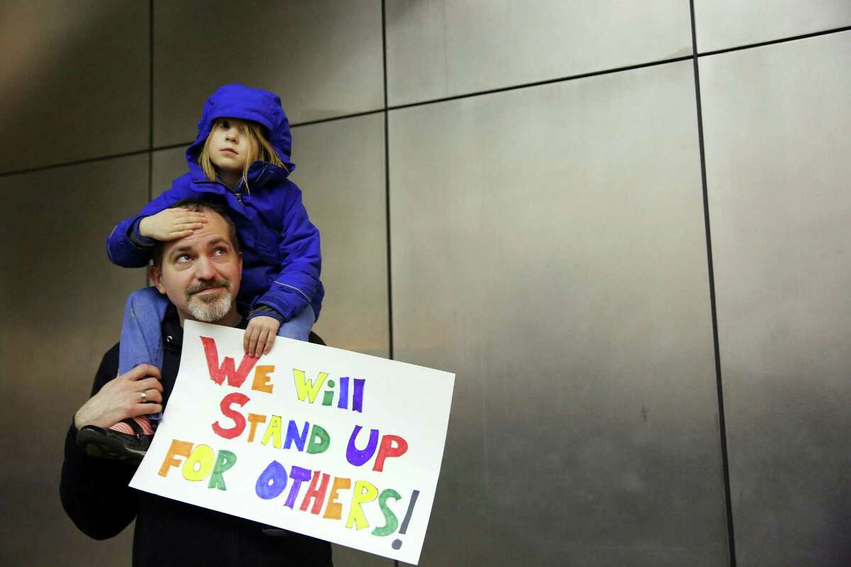 Matt Sernett holds his daughter Wade, 5, atop his shoulders, as more than 1,000 people gather at Seattle-Tacoma International Airport, to protest President Donald Trump's order that restricts immigration to the U.S., Saturday, Jan. 28, 2017, in Seattle. (Genna Martin/seattlepi.com via AP)