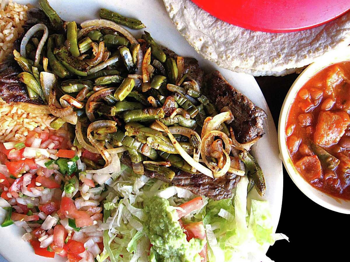 A carne asada plate from Taquería Potrillo. The plate comes with grilled onions, grilled nopales, rice, beans, guacamole and two tortillas.