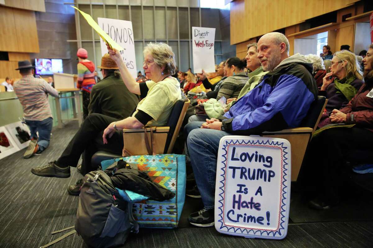 People hold signs in the chambers of Seattle City Hall, Wednesday morning, as the City Council holds a Finance Committee meeting on divesting about $3 billion in city money from Wells Fargo Bank because of the bank's involvement in the Dakota Access Pipeline.
