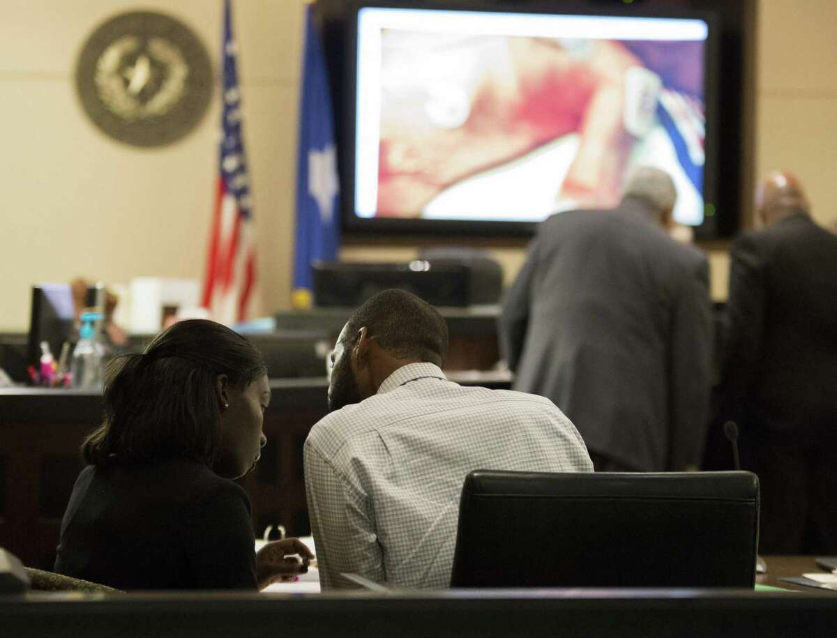 Marquita Johnson, left, and Qwalion Busby talk during their trial on Wednesday, Feb. 8, 2017, in the 290th State District Court in San Antonio. Johnson and Busby are charged with injury to a child, accused of withholding traditional medical treatment from their son, who later died as a result of illness. An image of their infant son is displayed as evidence on the screen in the background. (Darren Abate/For the San Antonio Express-News)