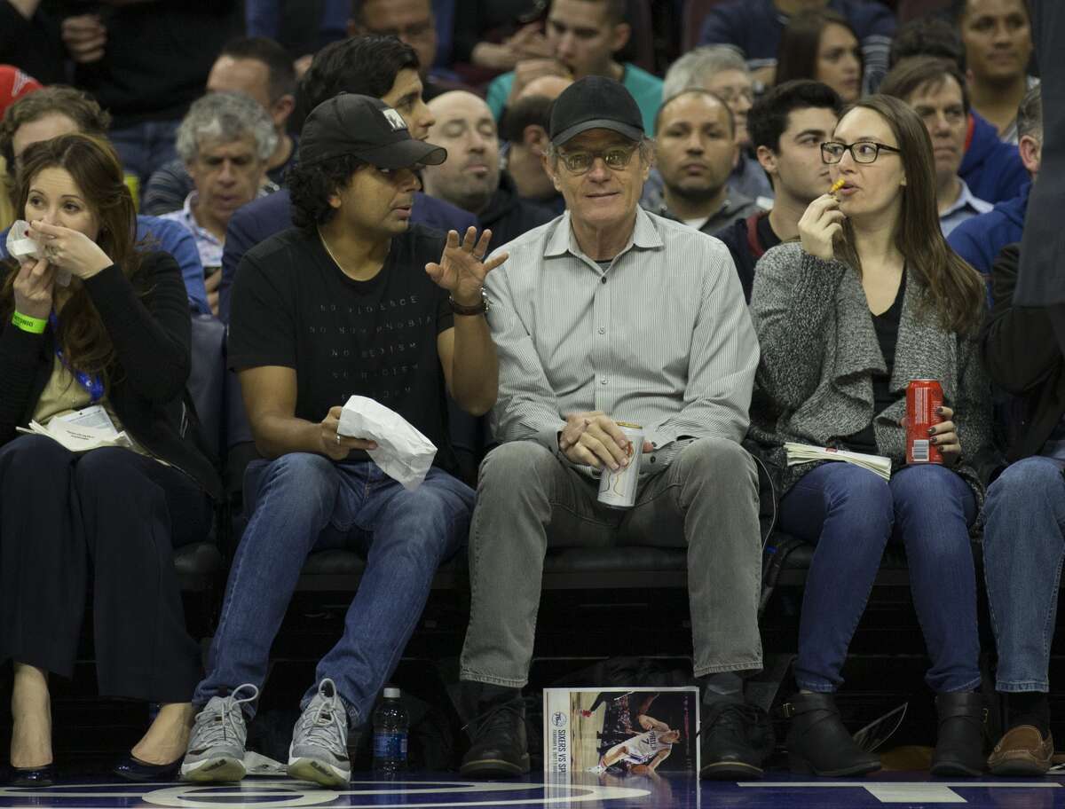 Director M. Night Shyamalan (possibly reenacting the alleged spank) talks to actor Bryan Cranston during the game between the San Antonio Spurs and Philadelphia 76ers at the Wells Fargo Center on February 8, 2017 in Philadelphia, Pennsylvania.