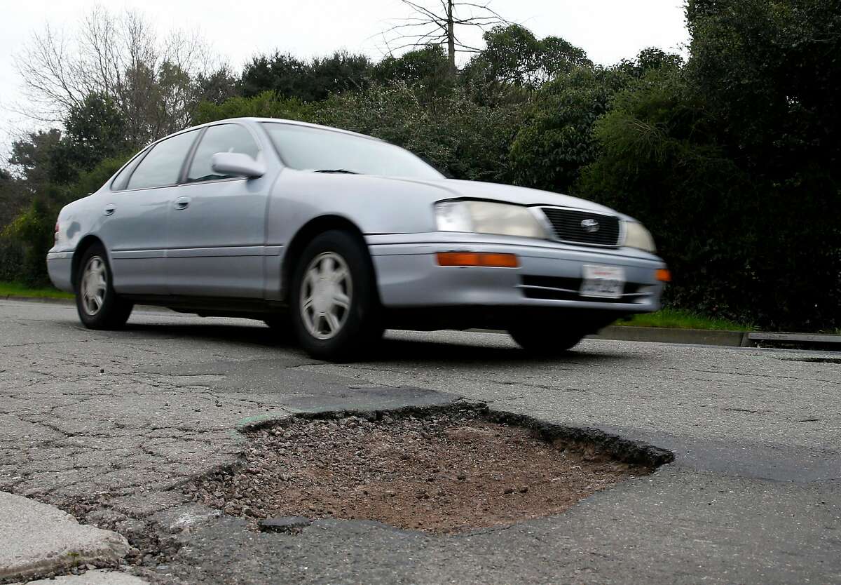 FILE-- A commuter slows down to drive past large potholes on Chatham Road in Oakland, Calif. on Wednesday, Feb. 15, 2017.  Roads throughout the Bay Area are slowly improving, according to a new report, and officials at the Metropolitan Transportation Commission are crediting an infusion of SB1 gas tax dollars for the gradual upward trend.