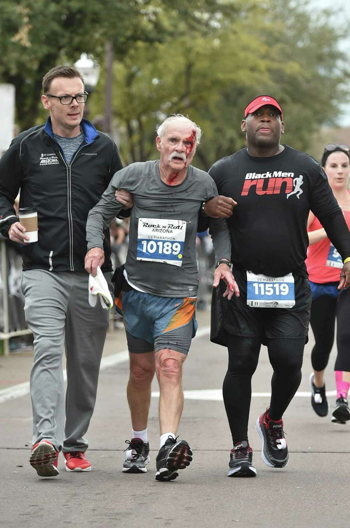 Colin Jackson (left) and San Antonio’s Nathanael Dillard (right) help injured runner John Wilkie during the Rock ‘n’ Roll Marathon in Phoenix on Jan. 15 2017.