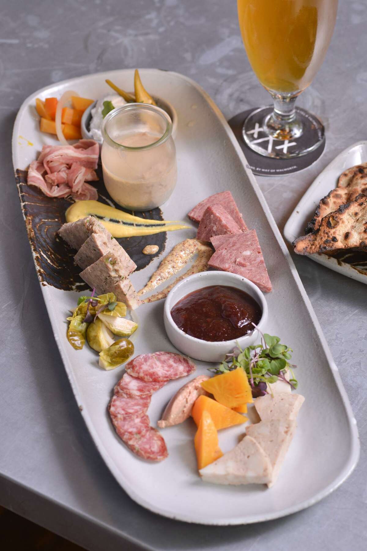 A charcuterie plate from Cured featuring mortadella, chicken liver mousse, jalapeño sauce, apple red wine jam, pickled Brussels sprouts, country style pork paté, smoked veal wurst, smoked lamb belly and whipped pork butter and beer flatbread.