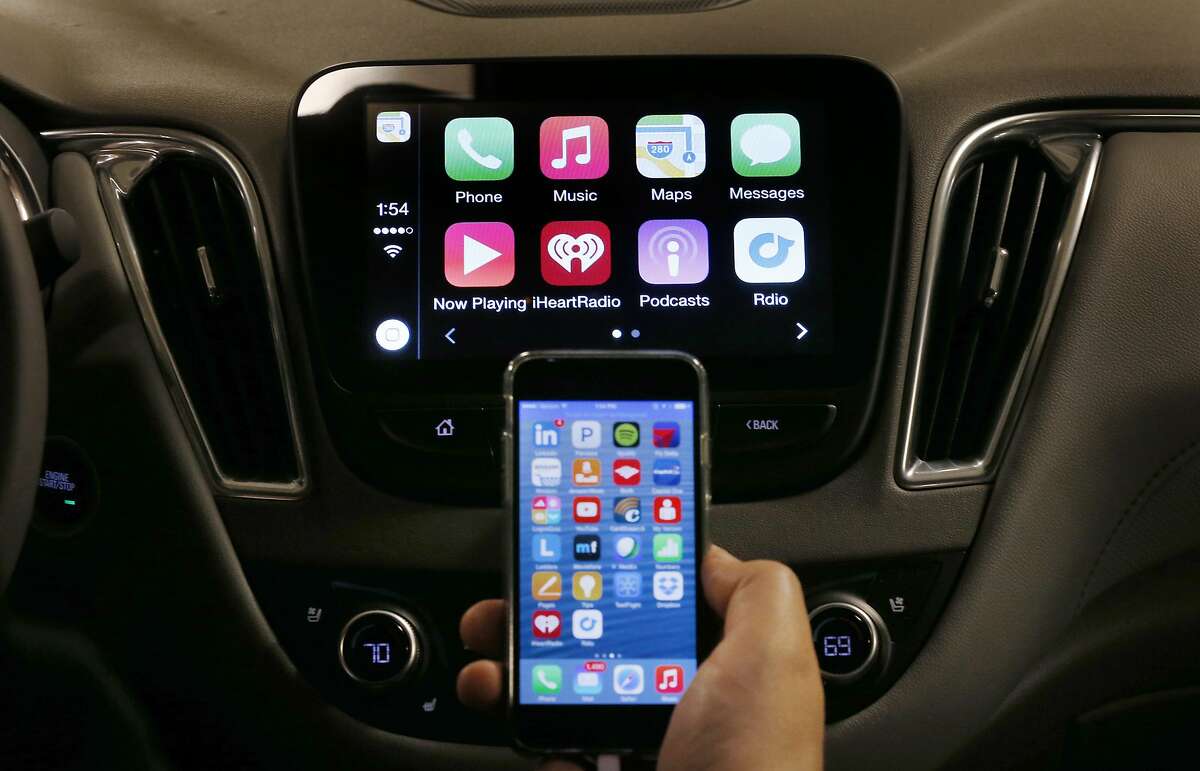 FILE - In this May 26, 2015 file photo, an iPhone is connected to a 2016 Chevrolet Malibu equipped with Apple CarPlay apps, displayed on the car's MyLink screen, top, during a demonstration in Detroit. The rapidly evolving in-car infotainment and navigation systems can be bewildering for all but the most tech-savvy car buyers. The average vehicle on U.S. roads is 11 years old; that means many people last went car shopping before iPhones were invented. (AP Photo/Paul Sancya)
