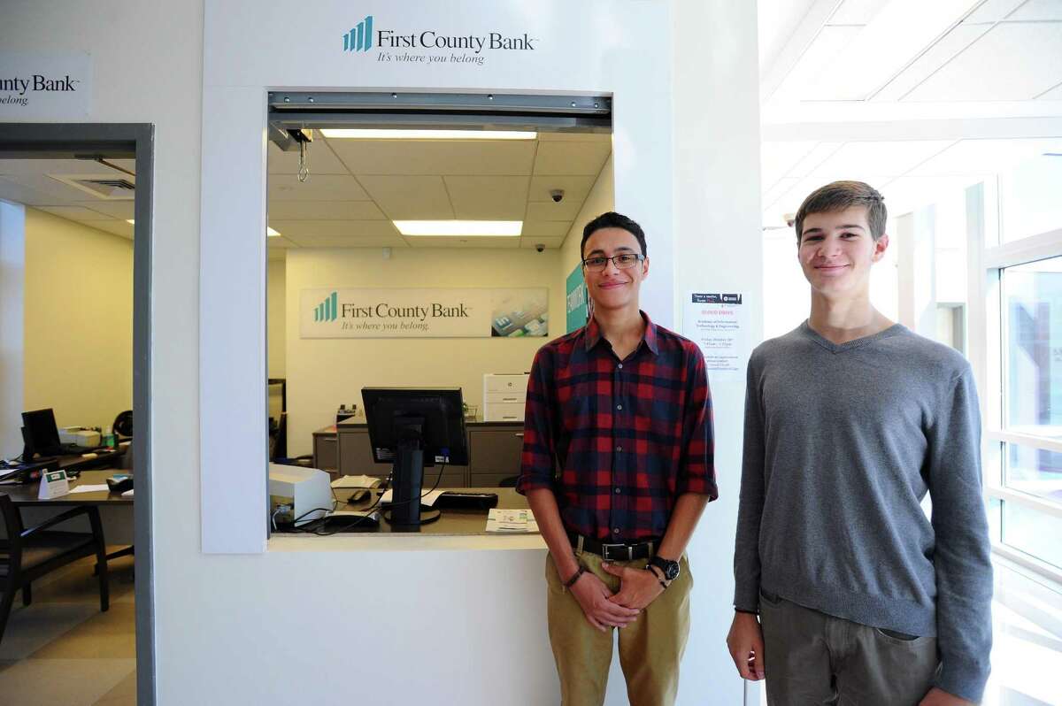 Academy of Information Technology and Engineering student interns Marco Lima, center, and Alex Graf pose outside First County Bank’s limited-access branch at AITE. Opened in 2016, the branch represents one of First County’s major financial-literacy initiatives.