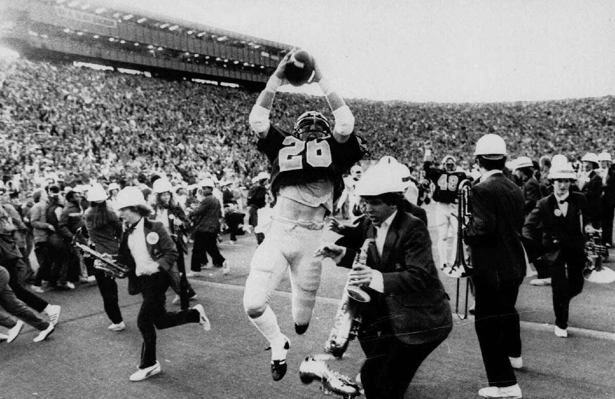 ** FILE ** California's Kevin Moen (26) leaps with the ball in the air after scoring Cal's winning touchdown while the Stanford band runs to get out of his way in Berkeley, Calif., in this Nov. 25, 1982 photo. When the Big Game rolls around each fall, Kevin Moen and Gary Tyrrell can't help being reminded about their roles in the wackiest four seconds in college football history. In 1982, Moen scored for California on the game-ending, five-lateral kickoff return known simply as The Play _ and Tyrrell was the Stanford band's trombone player who got leveled by Moen in the end zone. (AP Photo/Oakland Tribune/Robert Stinnett)