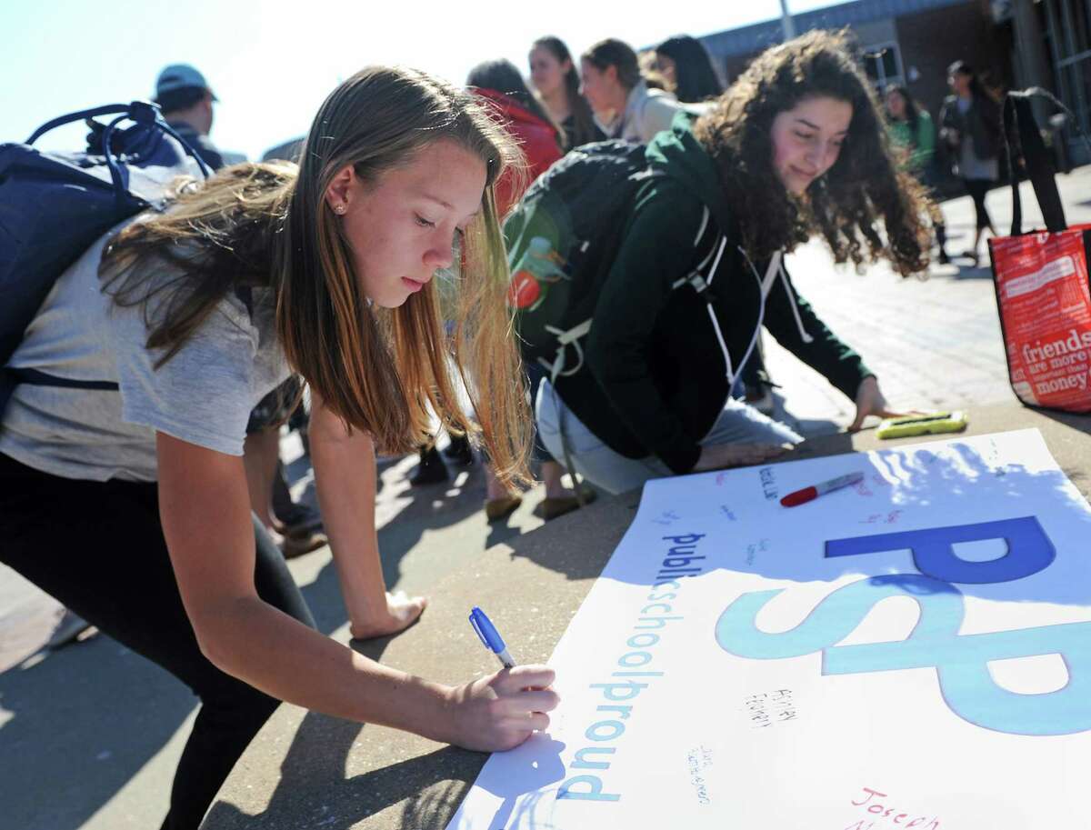 LEFT: GHS senior Maxine McMillan signs a poster in support of public schools at the #PublicSchoolProud rally in the courtyard at Greenwich High School in Greenwich. The rally, attended by dozens of student, was a reaction to the nomination of Betsy DeVos as Secretary of Education and the recent focus on charter schools, which divert funding from public school like GHS. Below: GHS senior Emma Himes applauds speakers.