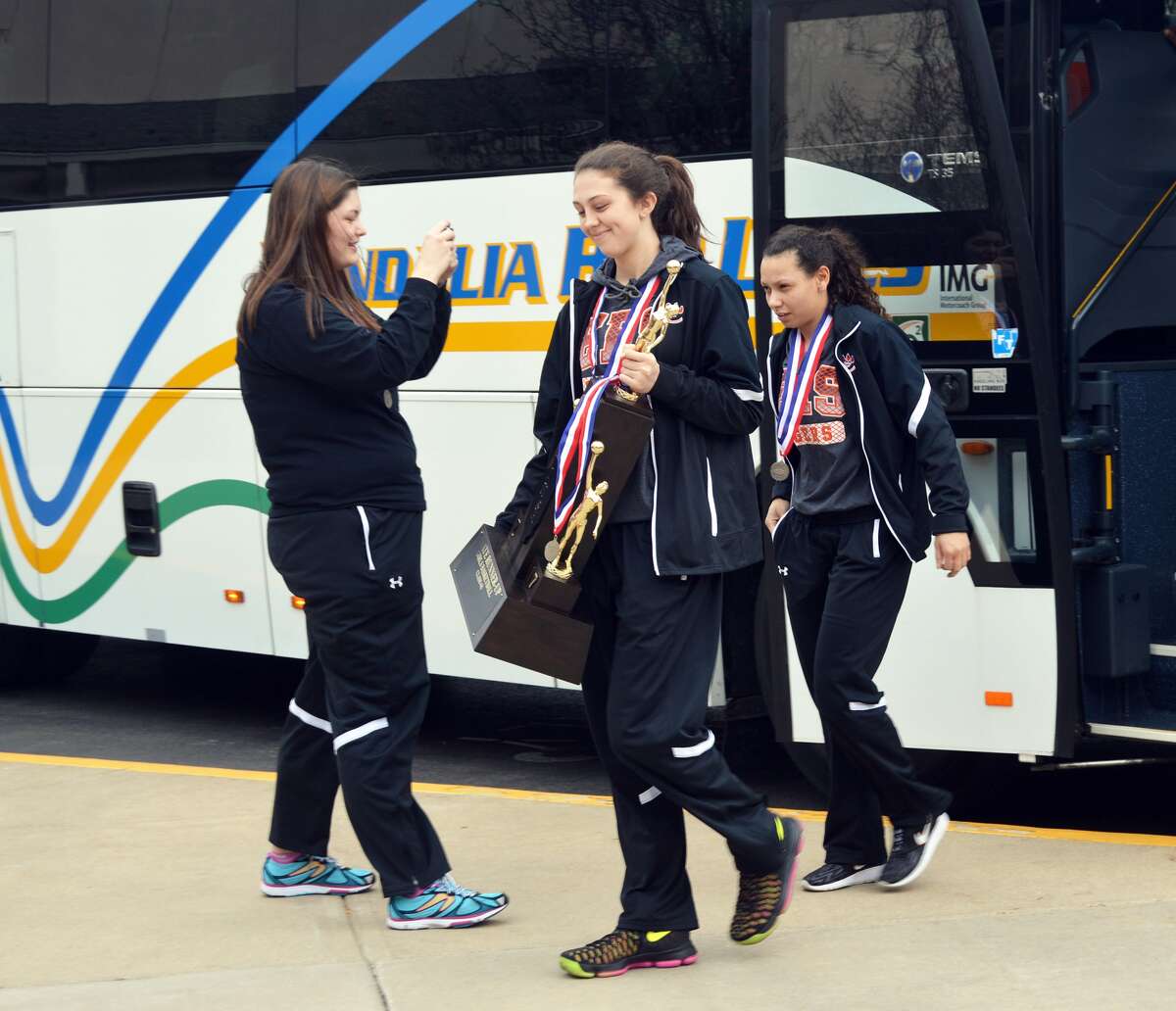 Edwardsville seniors Makenzie Silvey, center, and Jasmine Bishop walk off the bus with the second-place trophy on Sunday.