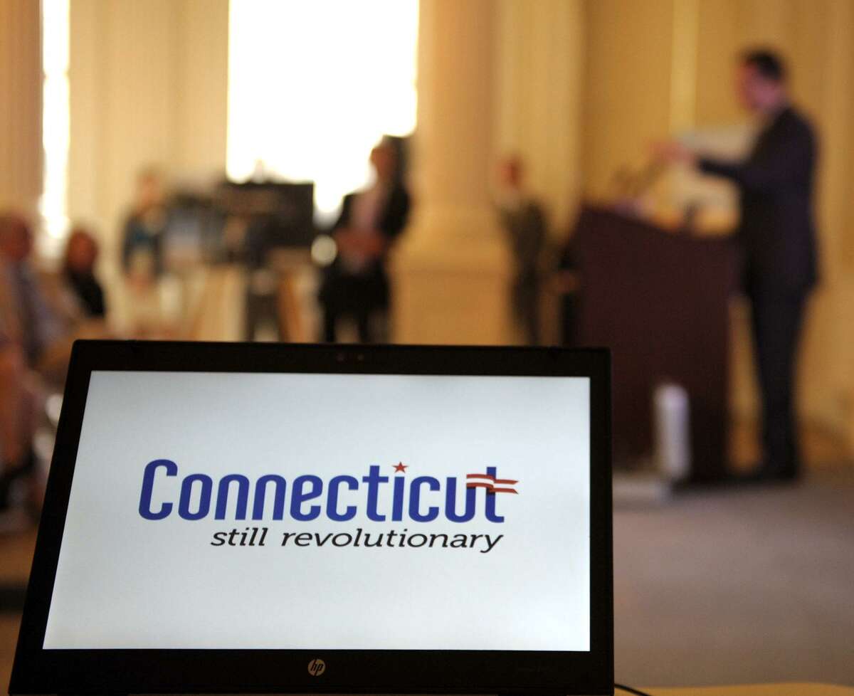 A "Still Revolutionary" logo is displayed on a laptop computer projecting onto a screen on stage as Connecticut Gov. Dannel P. Malloy speaks during an unveiling of a tourism branding campaign in 2012.