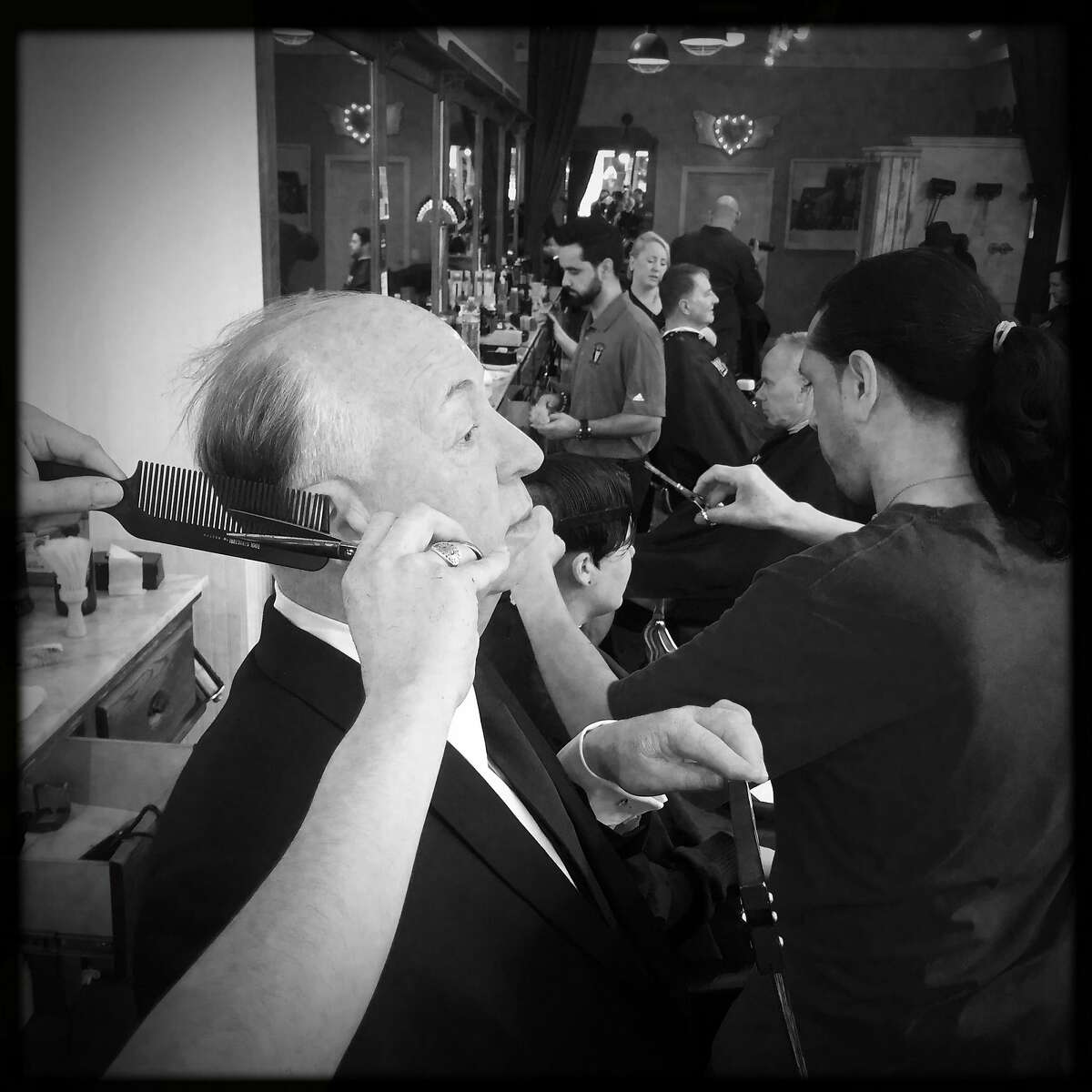 As Michael Casias (right) styles Joanna Pluhowski's hair, David Garcia pretends to trim the hair of a wax figure of Alfred Hitchcock that Madame Tussaud's brought to Peoples Barber in San Francisco, Calif., on Friday, March 10, 2017.