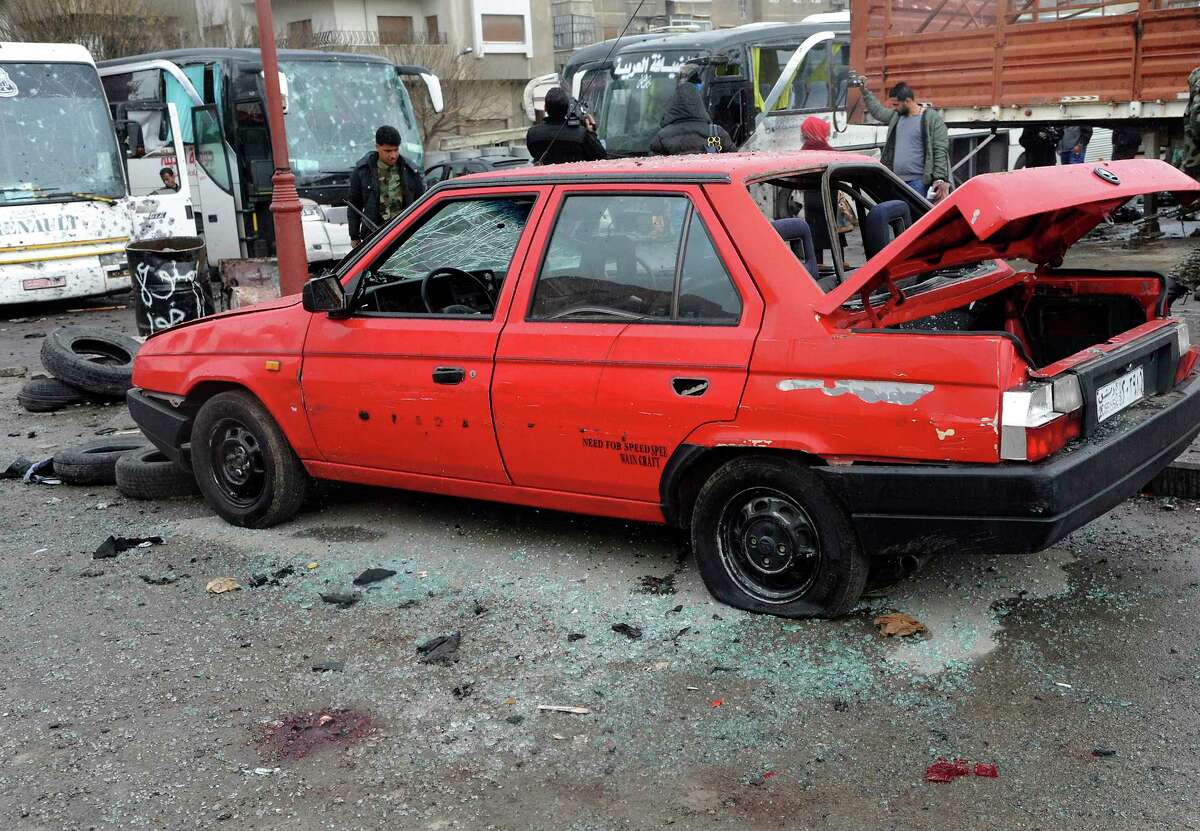 In this photo released by the Syrian official news agency SANA, people inspect the damage to a parking lot at the site of an attack by twin explosions in Damascus, Syria, Saturday, March 11, 2017. Twin explosions Saturday near religious shrines frequented by Shiite pilgrims in the Syrian capital Damascus killed dozens of people, Arab media and activists report. (SANA via AP) ORG XMIT: HAS105