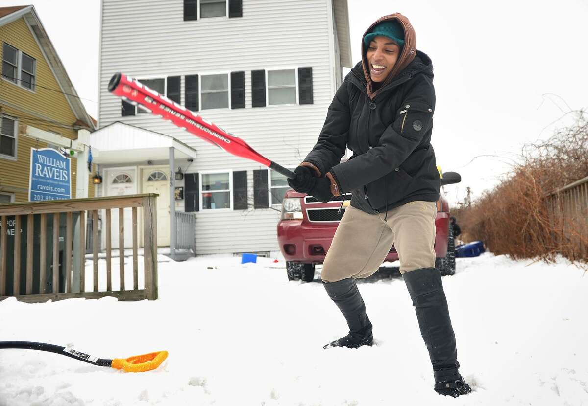 Athena Phipps uses an aluminum baseball bat to break through the ice at the end of her driveway on Union Street in Bridgeport on Wednesday, in the aftermath of the storm that dumped snow on the area on Tuesday.