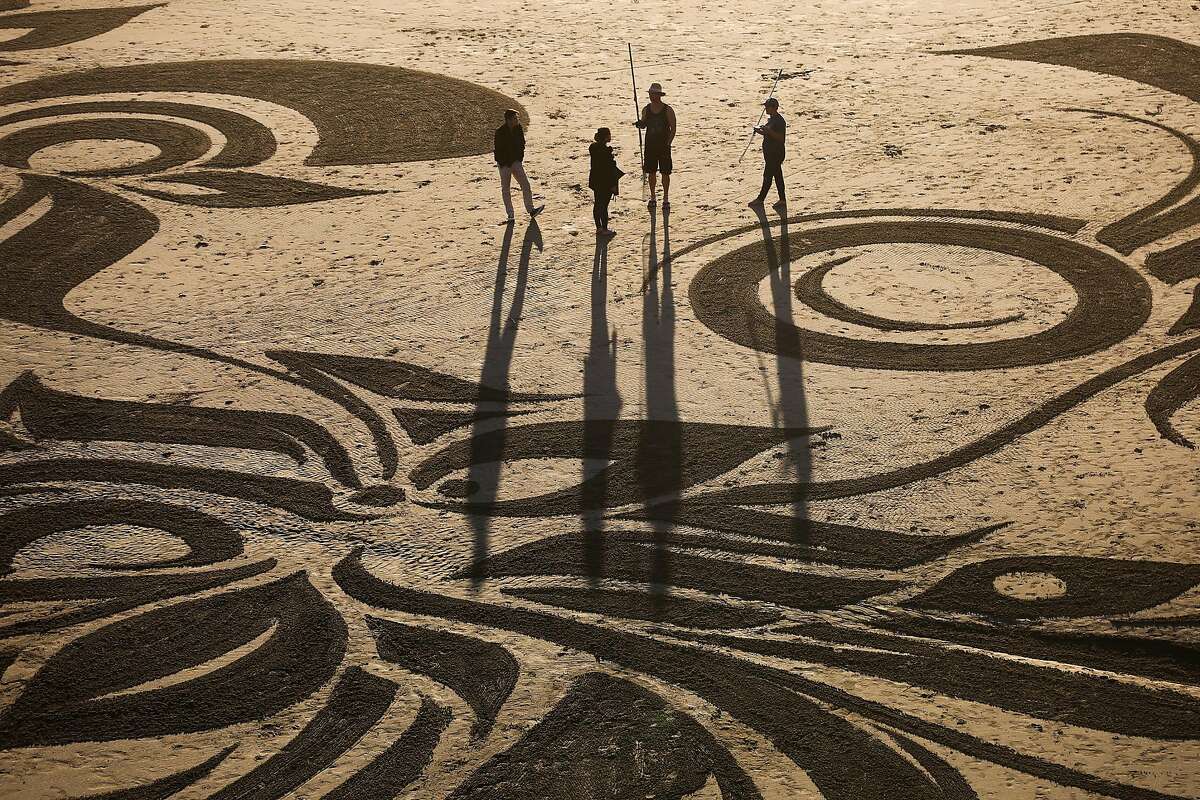 Artist Ian Ross (second from right) chats with people on the beach after making one of his artistic sand designs at Ocean Beach in San Francisco, California, on Tuesday, March 14, 2017.