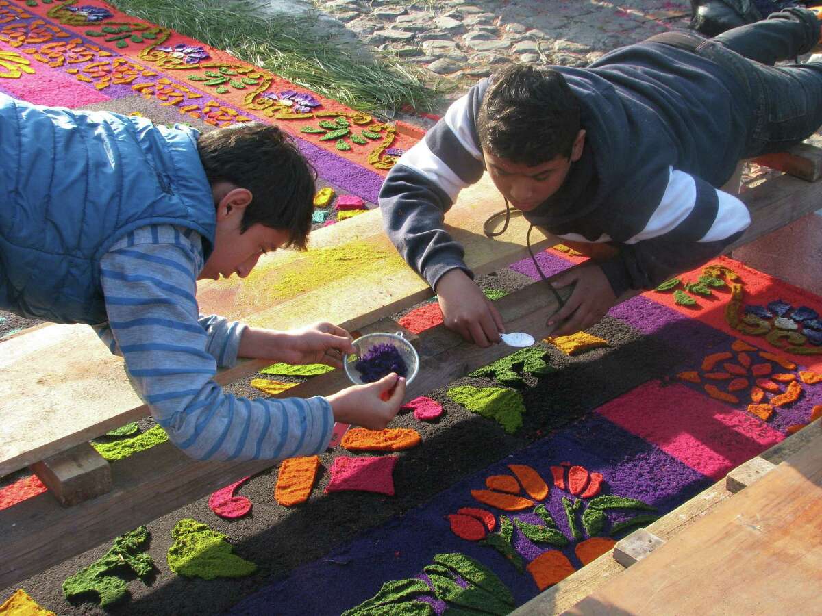Two men put the finishing touches on an elaborate sawdust pattern created on top of a cobblestone street in Antigua.﻿