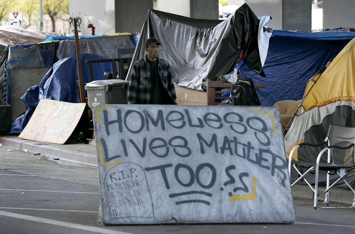 Shawn Moses walks behind the sign he created at a homeless encampment on Northgate Avenue below Interstate 980 in Oakland, Calif. on Thursday, March 23, 2017. Moses says he has lived in the camp for about three years, one of the longest established residents.