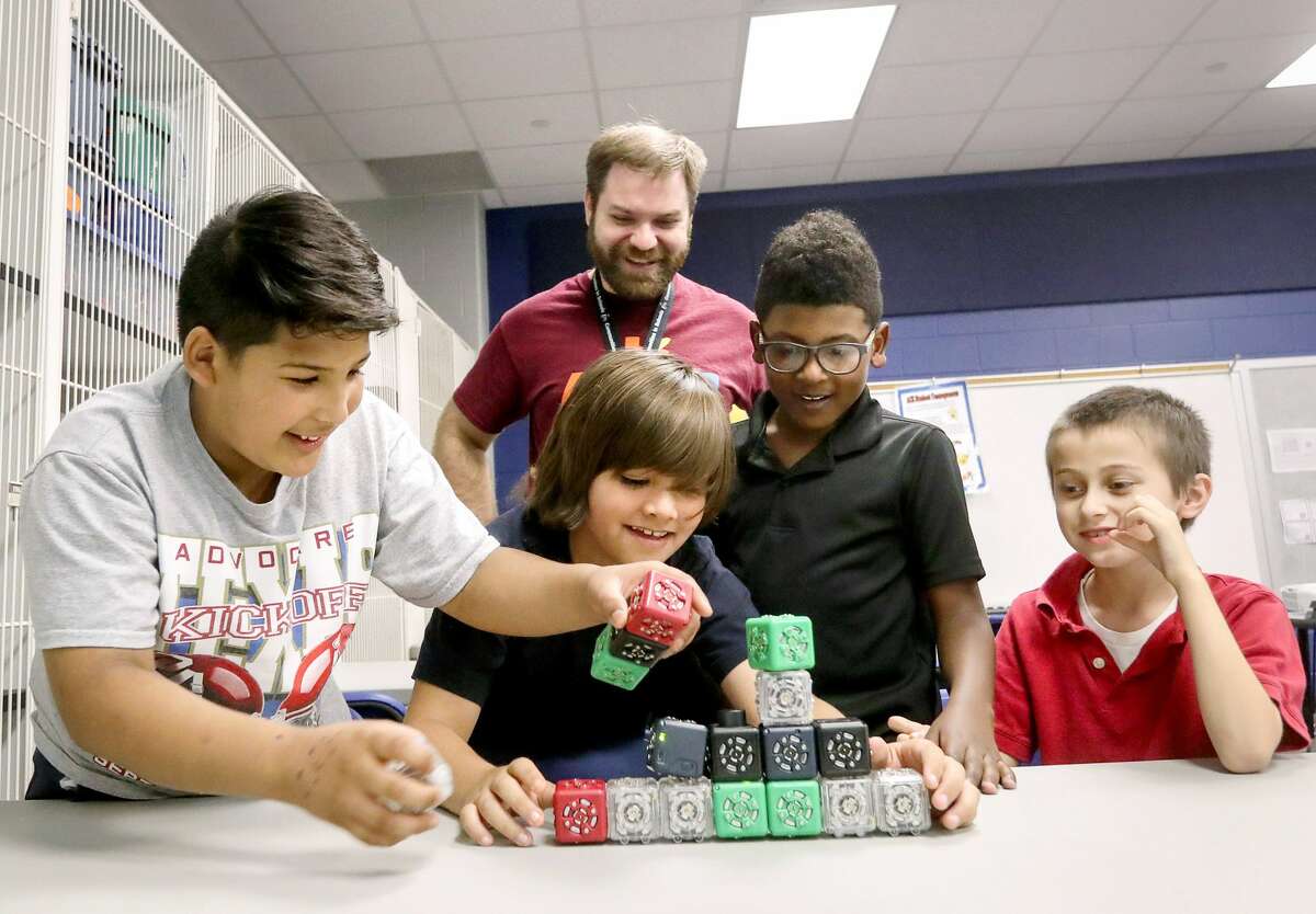 Travis Hayes, rear-center, an activity coordinator, looks on as Marc Pedraza, front from left, Joaquin Izaguirre, Roy Johnson and Aden Sitta play with robotic cubes during an after-school program at Magnolia Elementary School, Friday, March 24, 2017, in Pearland. When the cubes are combined with other ones, they move and perform tasks. Hayes uses the cubes to introduce the children to computer skills and coding. ( Jon Shapley / Houston Chronicle )