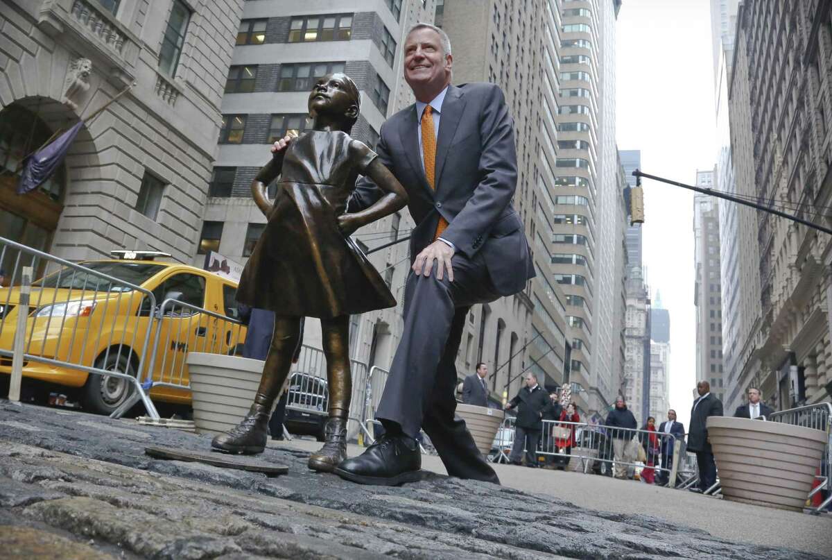 New York Mayor Bill de Blasio poses with the “Fearless Girl” statue before holding a news briefing Monday. De Blasio says the popular statue will be allowed to remain through February 2018.