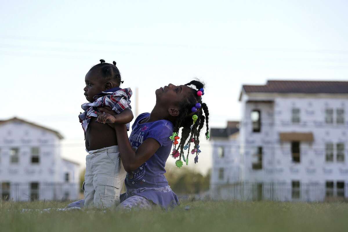 Sariyah Sheppard, 8, plays with Ge'ion Jennings, 6 months, on the field at Wheatley Middle School across from the East Meadows apartment complex under construction on March 31, 2016.