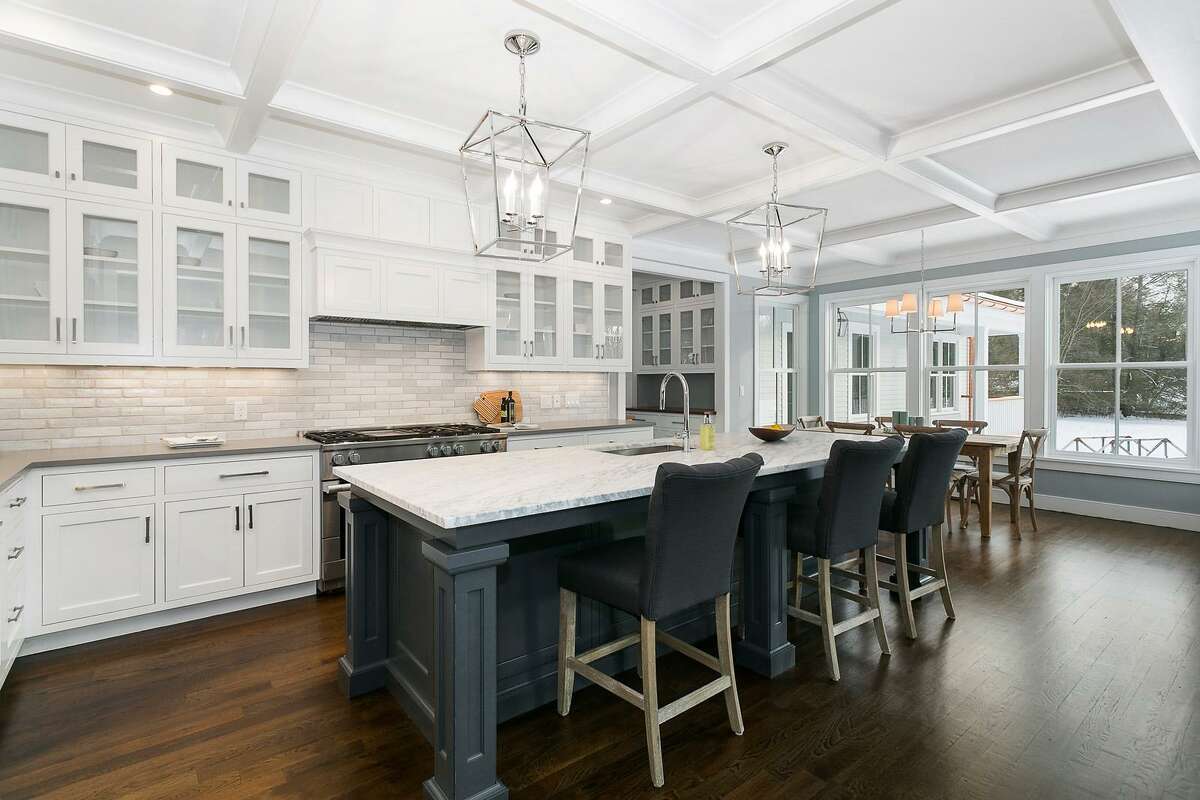 Features in the gourmet kitchen include a large casual eat-in or breakfast area, a center island topped with Carrera marble, coffered ceiling, quartzite counters, and high-end appliances, including a Miele six-burner range.
