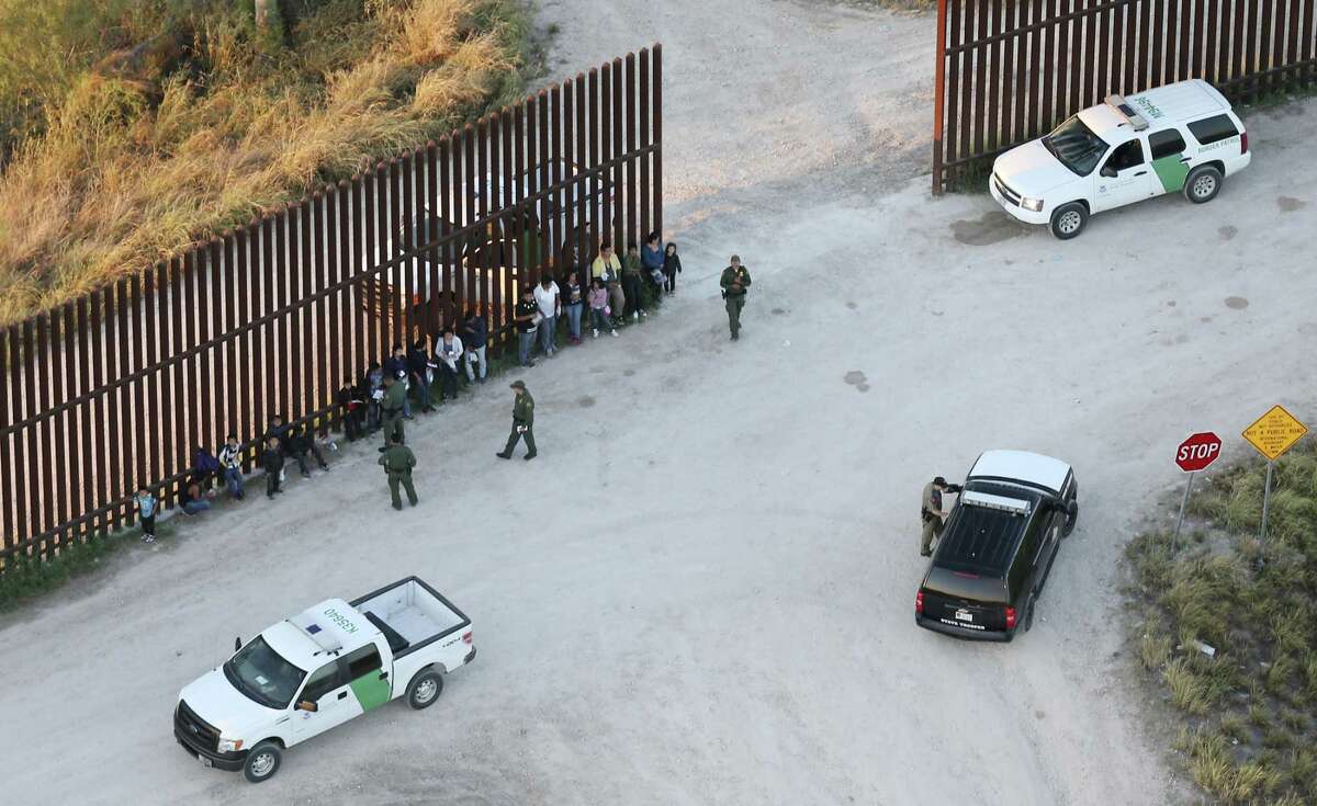 U.S. Border Patrol agents detain a group of immigrants, including children, by the U.S.-Mexico border wall near Penitas, Texas, Tuesday, Oct. 4, 2016. Also seen is a unit with the Texas Department of Public Safety.