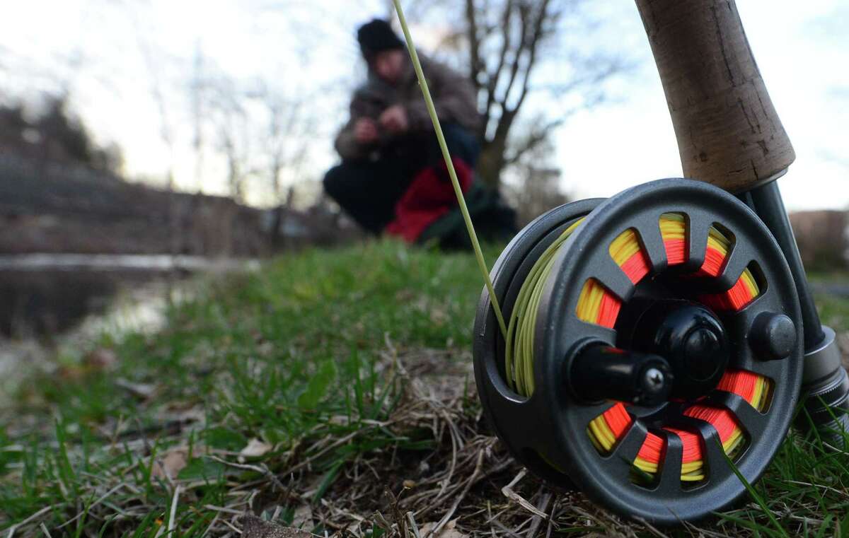 A fly casting reel sits idle as Norwalk resident Jeremy Williams baits his hook while fishing for trout on the Norwalk River during opening day Saturday, April 8, 2017, in Wilton, Conn.
