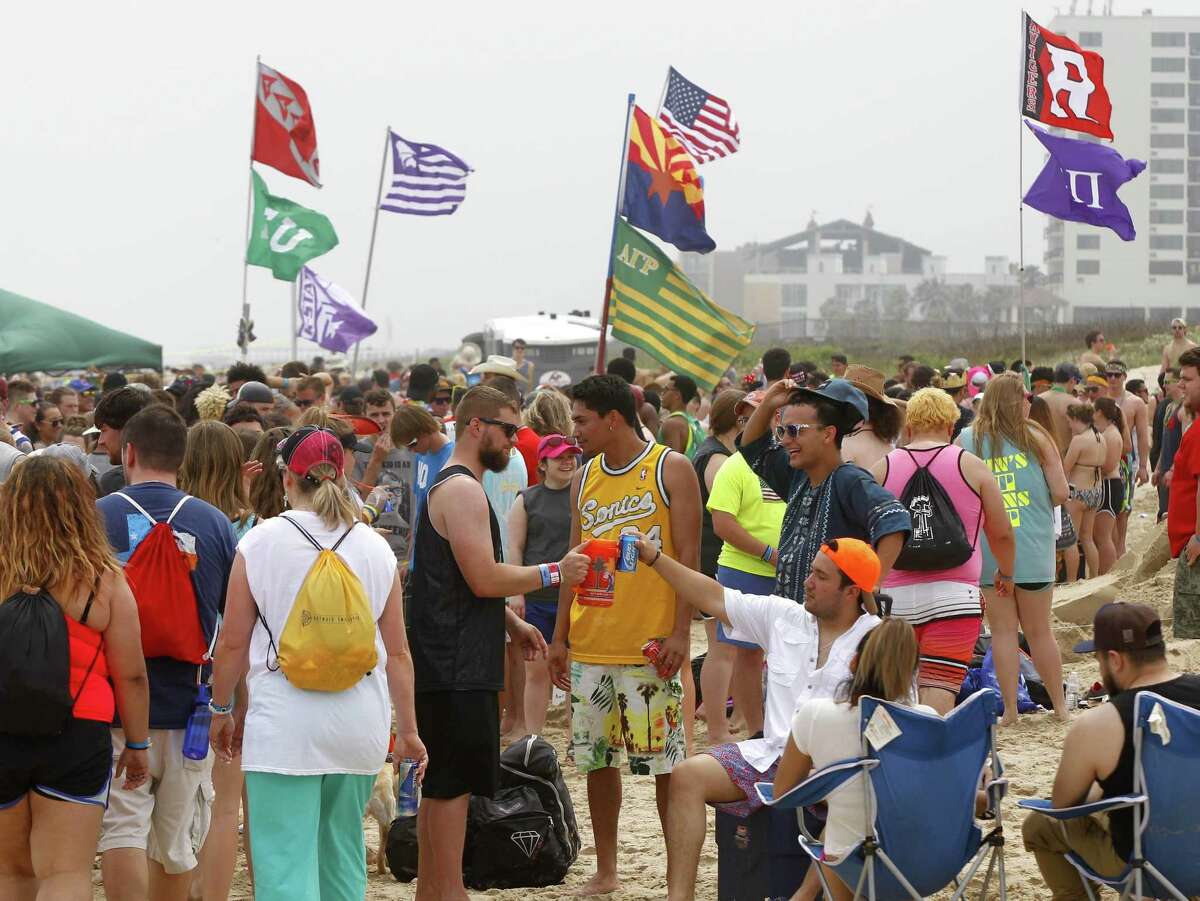 Spring breakers sit on the beach under flags from their universities Thursday, March 17, 2016, at South Padre Island, Texas. (Nathan Lambrecht/The Monitor via AP) MAGS OUT; TV OUT; MANDATORY CREDIT