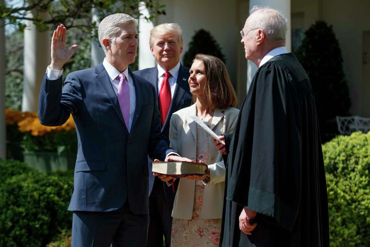 With President Donald Trump in the background, Supreme Court Justice Anthony Kennedy re-enacts the swearing-in of Judge Neil Gorsuch on Monday. ﻿