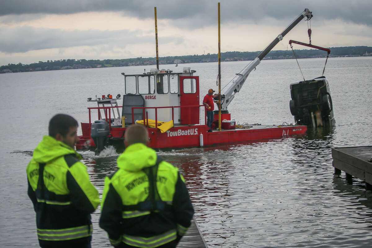 Two firefighters with North Montgomery County Fire look on as a submerged truck is towed out of Lake Conroe by TowBoatUS on Tuesday at the FM 830 Boat Ramp.