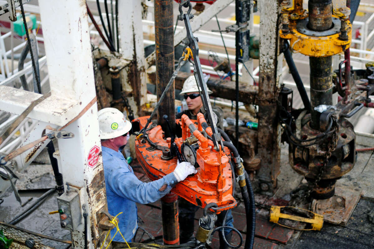 Kevin Giddings, left, and Noe Olvera, right, add a section of casing down a vertical well on the floor of Trinidad Rig 433 on Nov. 2, 2016, in Midland County.