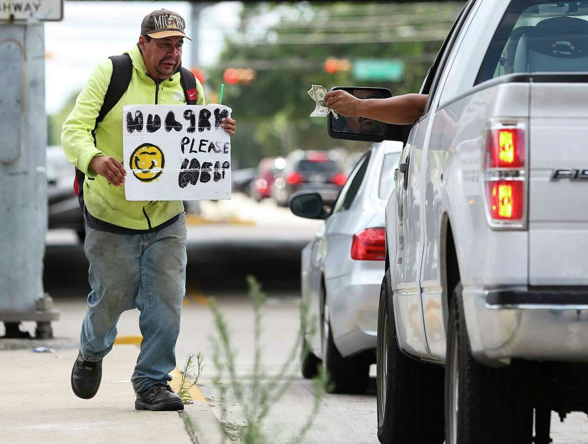A driver hands a few dollars to Andrew Quintanilla at a Southwest Freeway feeder road intersection ﻿Friday. Because of a new ordinance prohibiting blocking medians and other spaces, seeking donations this way could be subject to a Class C misdemeanor. ﻿