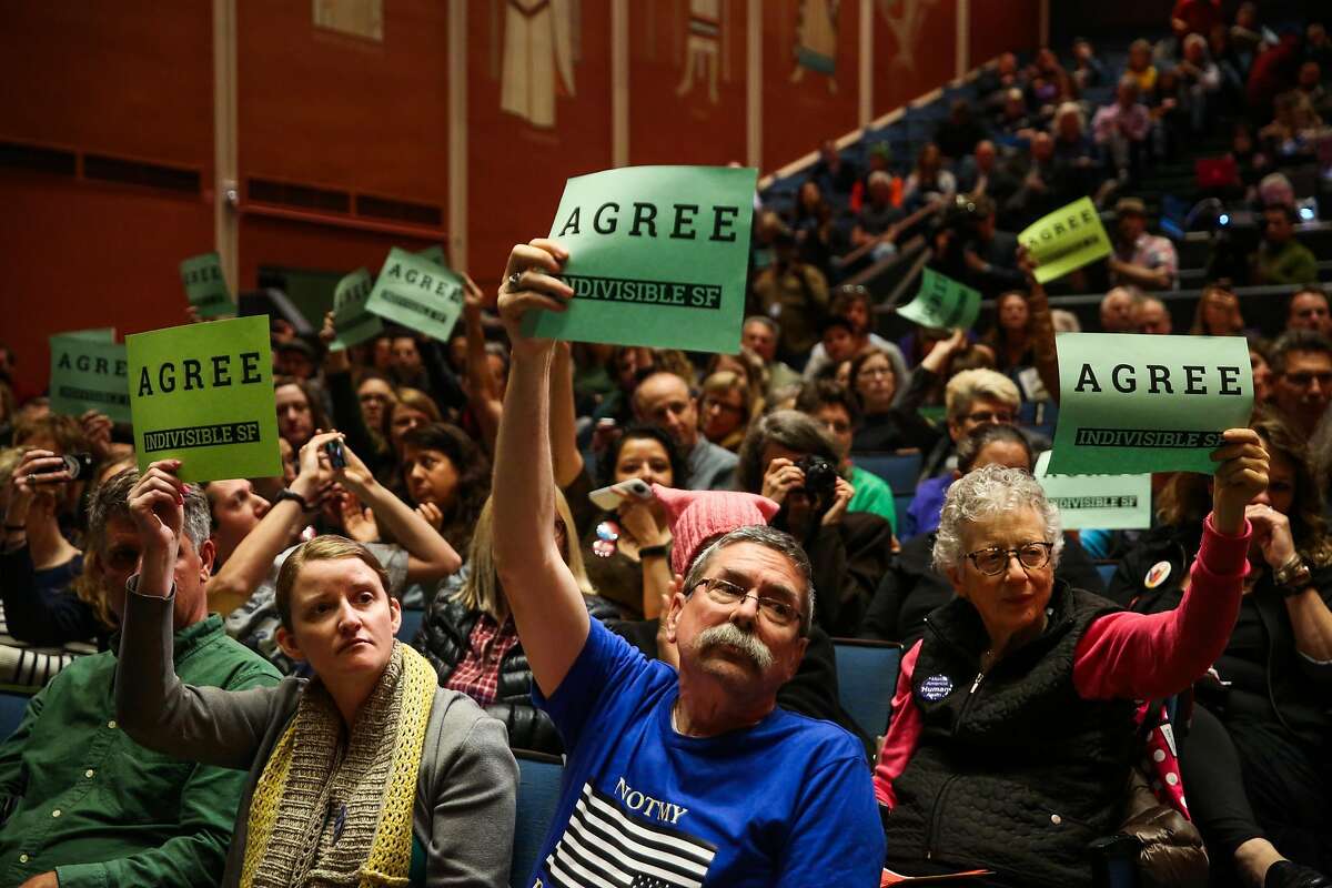 (左至右)Mimi Main和Greg Pennington(中)举着标语，因为他们同意参议员Dianne Feinstein于2017年4月17日星期一在加利福尼亚州旧金山苏格兰仪式共济会中心举行的市政厅会议上发表的评论。
