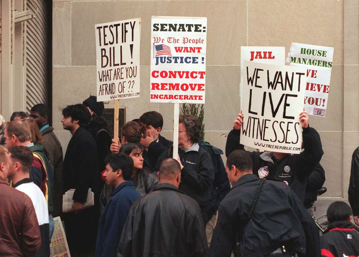 Protesters demanding live witness testimony at US President Bill Clinton's impeachment trial and his removal from office wave posters in front of the Mayflower Hotel on January 30, 1998 in Washington, DC, before the arrival of former White House intern Monica Lewinsky.