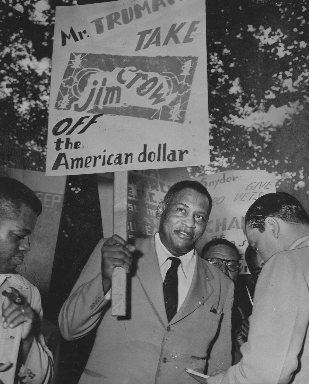 Paul Robeson, actor and singer, in a protest march outside the White House, with a banner requesting that President Truman take Jim Crow off the American dollar.