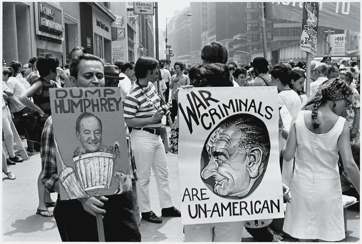 Protestors hold signs at an anti-war rally in New York, New York, Fall 1968. The visible signs read 'Dump Humphrey,' which shows a photograph American Vice President Hubert Humphrey in a garbage can, and 'War Criminals are Un-American,' which shows a caricature of Vice President Humphrey.