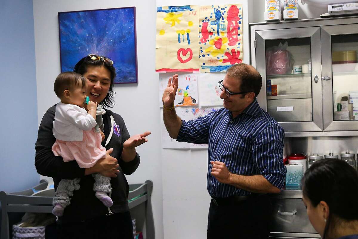 Dr. Oded Herbsman (center) gives Hazel Hua (left), 12 months, a high five after getting a vaccination with parents David Hua (left) and Stephanie Hua (right), in San Francisco, California, on Monday, April 17, 2017.