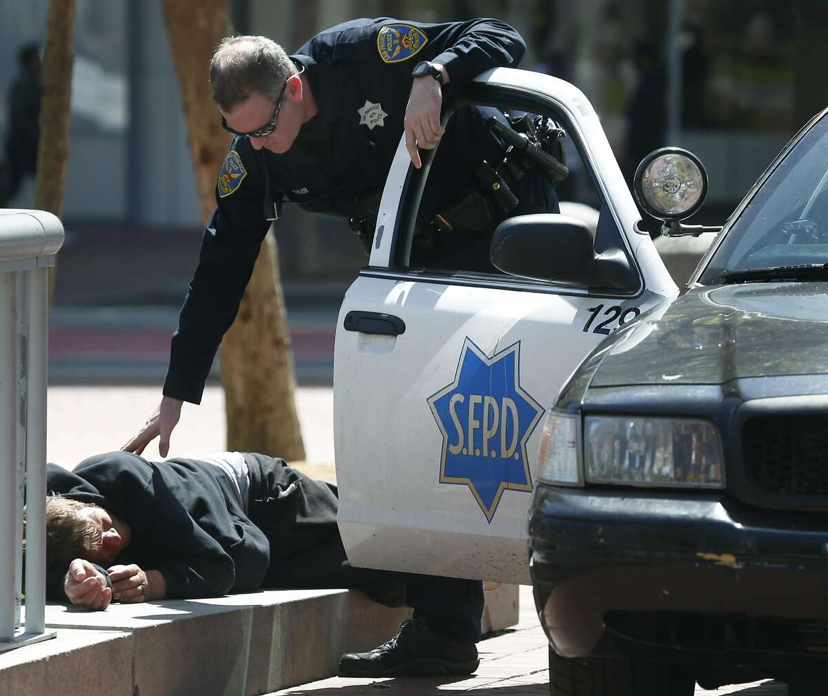 A police officer checks on the well being of a man lying down at United Nations Plaza in San Francisco, Calif. on Thursday, April 20, 2017. The city may soon become the first in the United States to open a safe injection site for intravenous drug users.