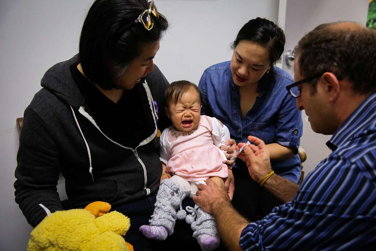 Dr. Oded Herbsman (right) vaccinates baby Hazel Hua, 12 months, while parents David Hua (left) and Stephanie Hua (second from right) hold her close, in San Francisco, California, on Monday, April 17, 2017.